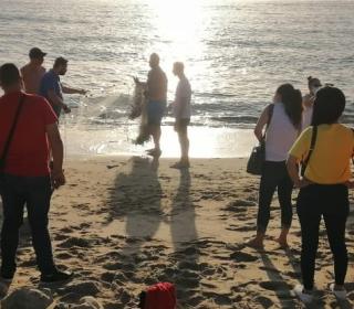 Two men prepare to cast a fishing net into the ocean as a several people on the beach look on.