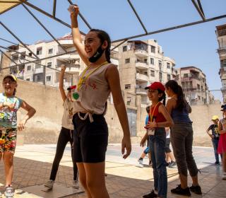 A girl holds up a ball while other children play around her in a courtyard.