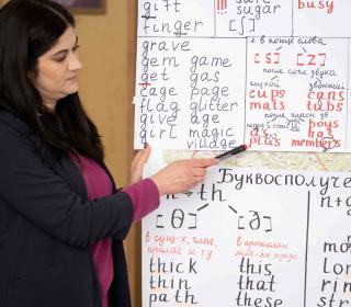 A woman points at a whiteboard covered in English and Ukrainian words.