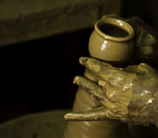 A potter's hands covered with wet clay and shaping a vessel on the pottery wheel in India.