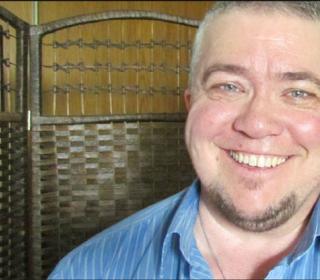 Jordan Sullivan, a White man with blue eyes and a goatee, smiles brightly at the camera.