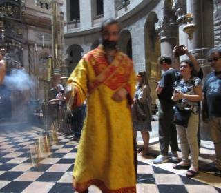 An Eastern Orthodox priest in an orange robe swings a censor in The Church of the Holy Sepulchre in Jerusalem.