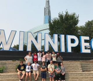 The group of GC43 Pilgrims gather around a huge Winnipeg sign during their visit to the Conference of Manitoba and Northwestern Ontario