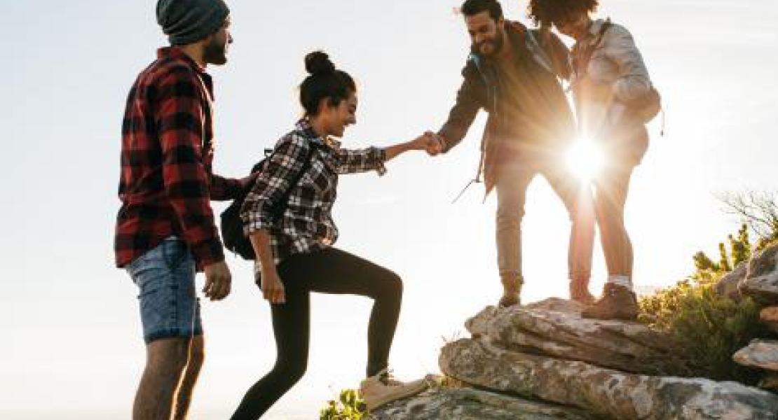 A group helping each other climb over rocks with the sun in the background