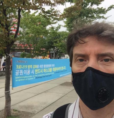 The author, John Egger, wears a pandemic face mask as he takes a selfie before a sign written in Korean in Seoul, Korea.