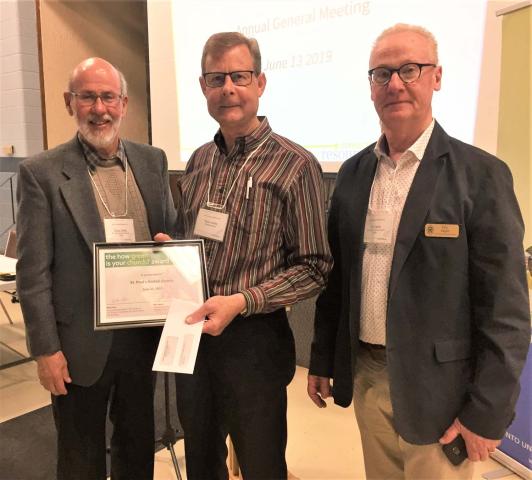 Three men hold a plaque and cheque their church was awarded for reaching the top green church level.