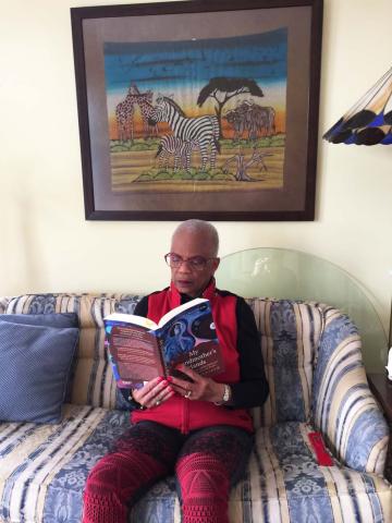 A Black woman sits on a couch reading a book, beneath a picture of a zebra.