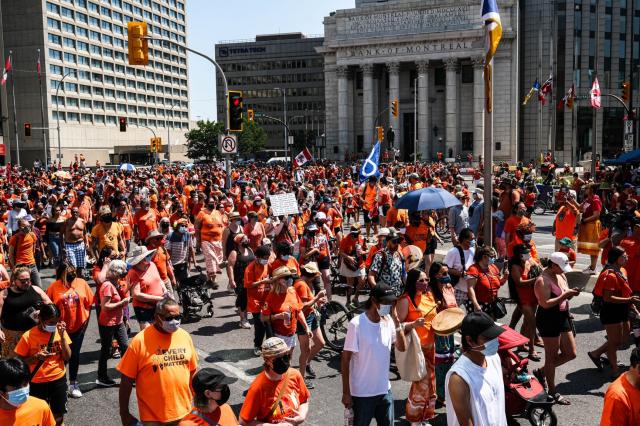 Rally participants hold up signs and wear orange shirts as they march down Portage Avenue, Winnipeg