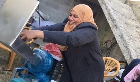 Image: A smiling Palestinian woman works beside the chute of a steel machine.