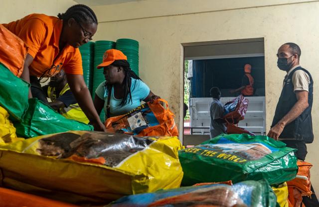 Two women in Haiti unload filled bags from the back of a pickup truck