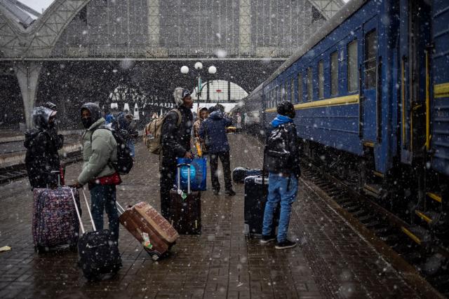 Several Nigerian students with their luggage stand in front of a train at the Lviv station in a snowfall.