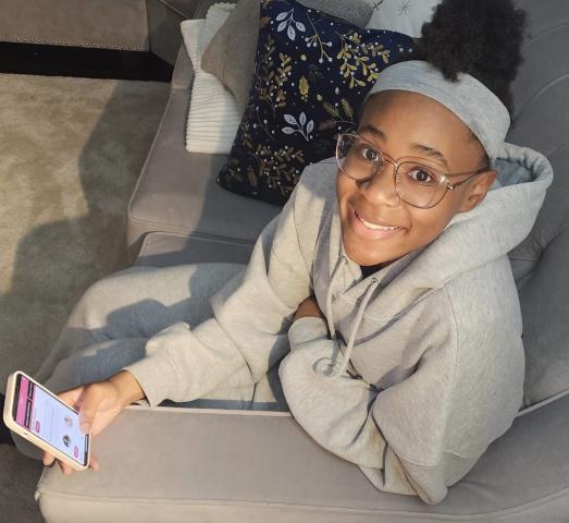 Jonisha Lewinson, a teenage girl dressed in a grey hoodie, sits on a couch holding her smartphone 