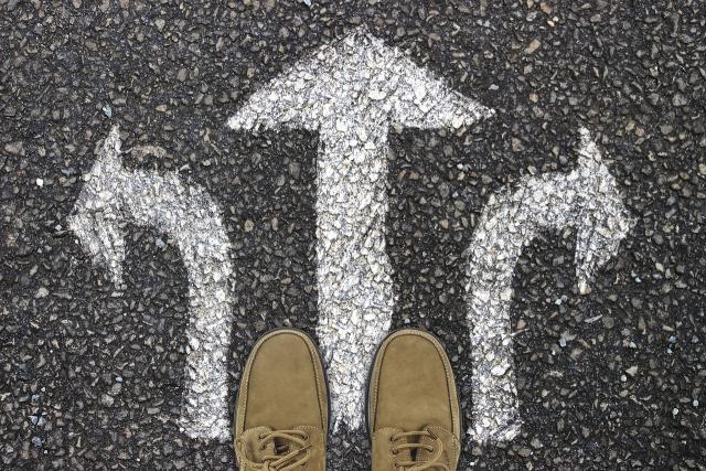 The viewer is looking down, at their feet, which at standing on a sign painted on the street with three arrows pointing in different directions.