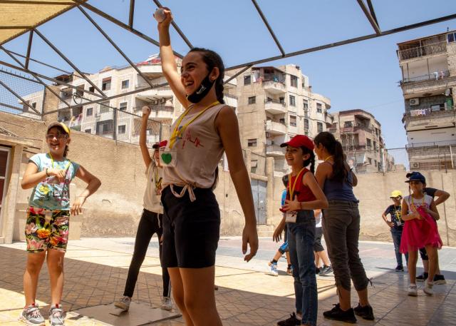 A girl holds up a ball while other children play around her in a courtyard.