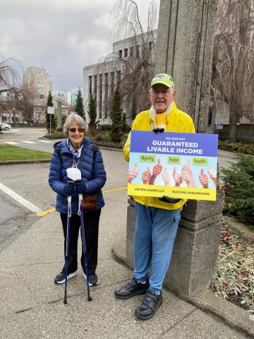 Two people hold up signs supporting a guaranteed livable income.