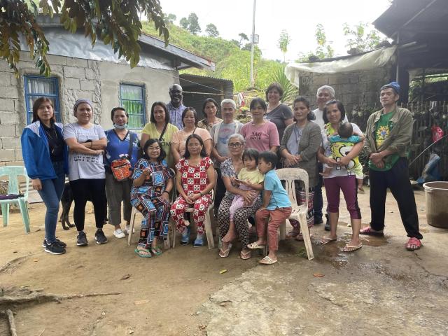 A large group of village residents stand with Moderator Carmen Lansdowne and Rev. Dr. Japhet Ndhlovu in a Filipino mountain village.