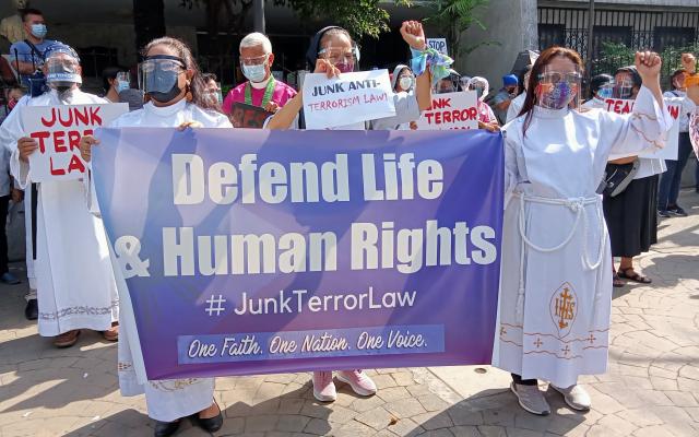 Several people at a protest hold up signs and a banner saying Defend Life & Human Rights