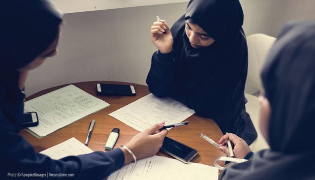 Three young Muslim girls sit around a table discussing their homework.