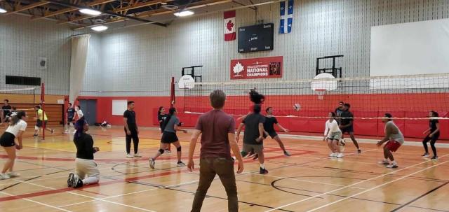 A group of young people from Madagascar playing volleyball in an indoor gym. Cameron Fraser is in the left corner, preparing to hit the ball