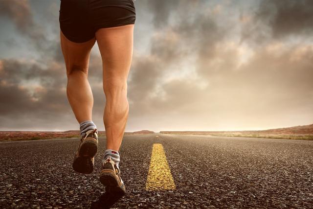 A view from the street level, showing the legs of a person in shorts jogging down a long road.