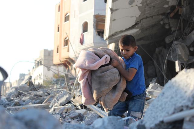 A child carrying a blanket walking through rubble in Gaza