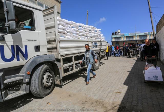 A large UN aid truck is loaded with bags in front of a refugee camp.