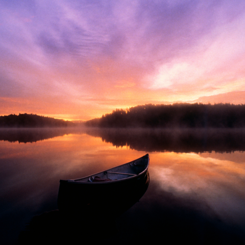 Canoe pulled up on shore of lake at sunset.