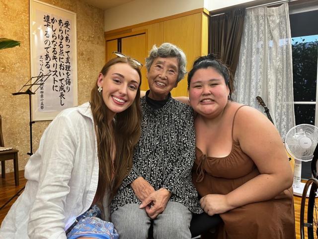 An older Japanese woman seated between two young women, all three smiling.