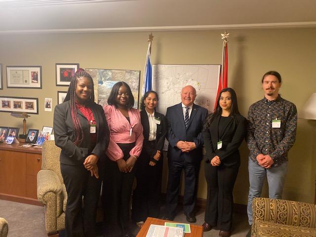 Five young people pose with a man in his office.