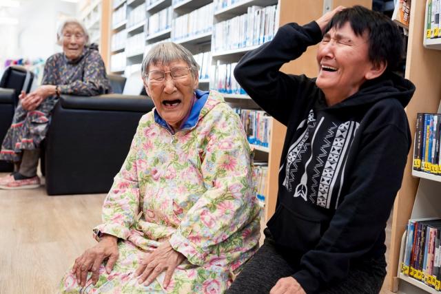 Two elderly Inuinnait women laugh along with a younger woman.