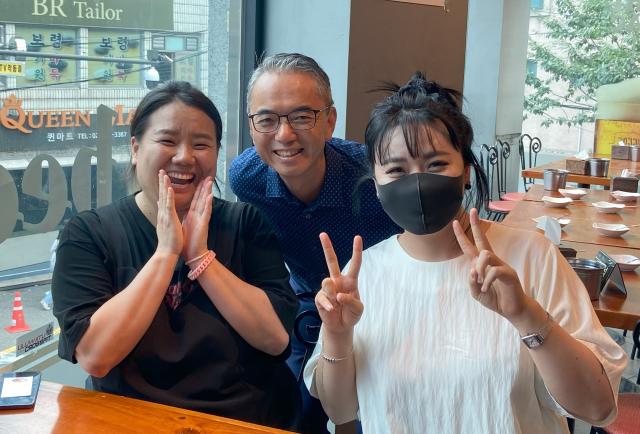 Two women and a man smile at the camera. They're at a table in a restaurant.