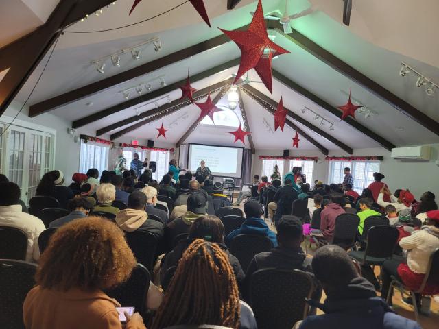 Young people fill a large room watching a presentation at the front.