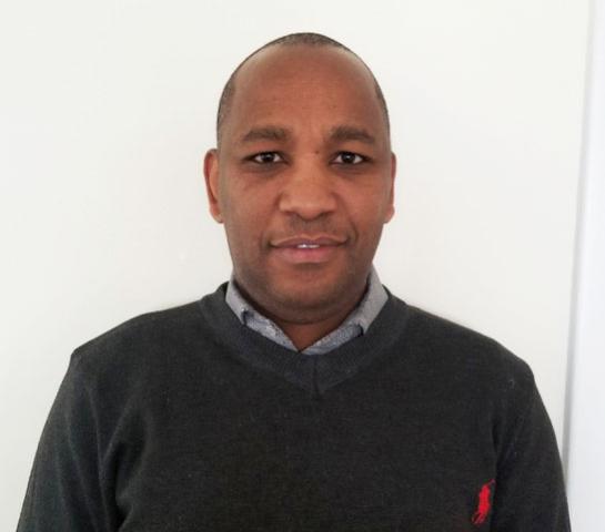 A portrait of Rev. Andrew Kinoti Lairenge, a middle-aged Black man with very short hair and kind eyes. Slightly smiling.