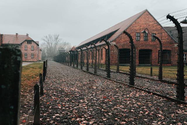 A photo of the brick buildings of Auschwitz concentration camp in Poland, surrounded by high barbed wire fencing.