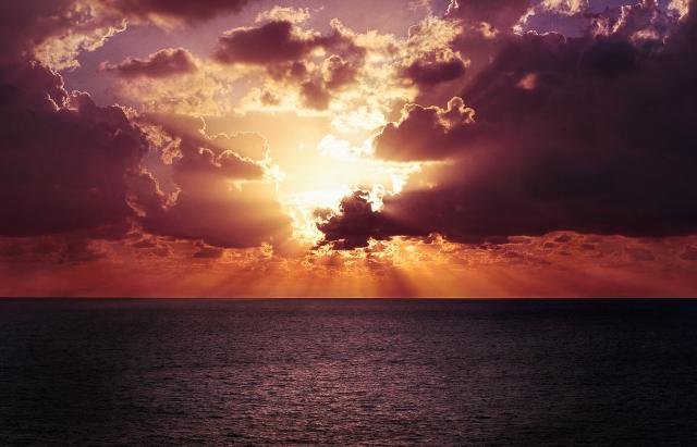 A brilliant orange-red sunrise over a large body of water is partially obscured by dark clouds.